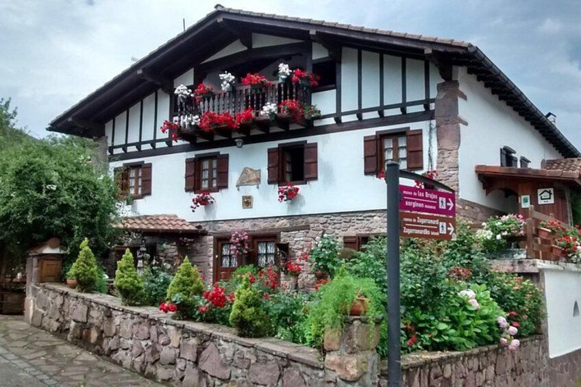 A traditional Alpine chalet with a balcony adorned with red flowers, stone walls, and a signpost indicating directions. 3