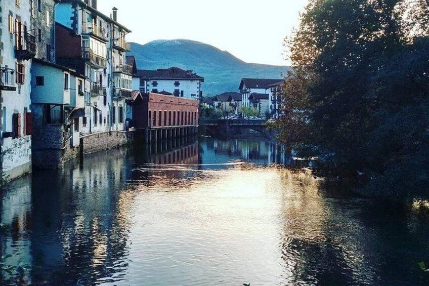 A calm river with buildings on the left bank, a bridge in the middle, and a mountain in the background. 2