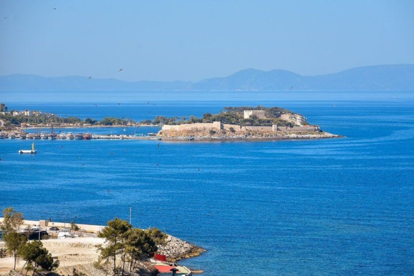 A coastal landscape with a prominent island featuring a fortified structure, calm blue waters, and distant mountains. 2