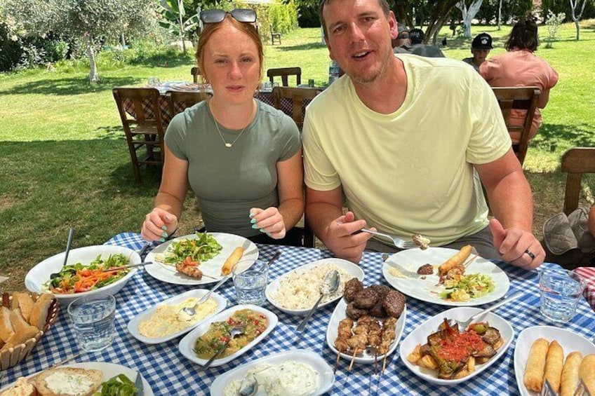 A couple dining outdoors with various dishes on a checkered tablecloth. 4