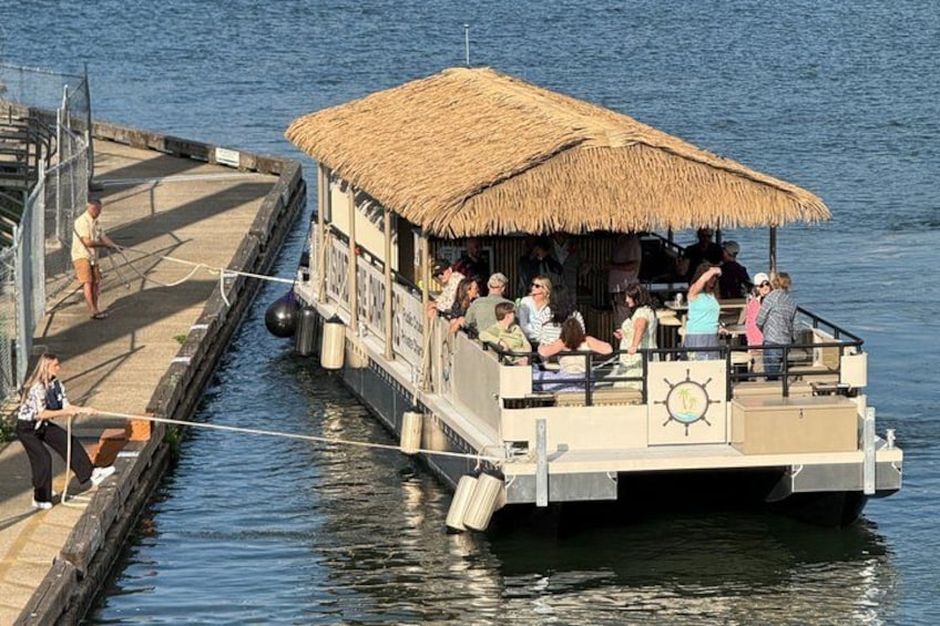 A boat with a thatched roof docked at a pier, people on board, and a calm water body. 5