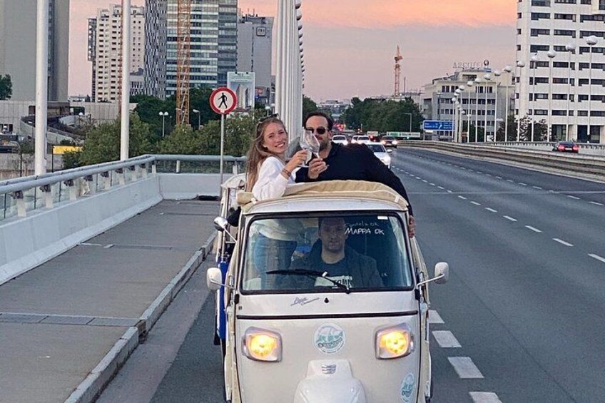 A vintage car on a bridge with a city skyline in the background. 1