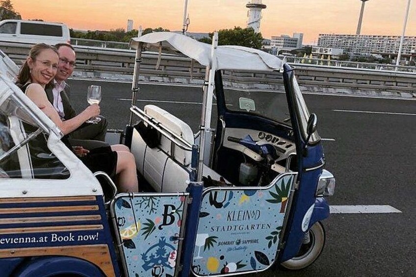 A couple in a city car with a blue and white design, parked on a road with a sunset in the background. 2