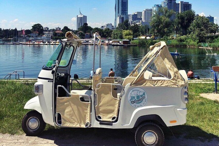 A white golf cart with a canopy, parked by a waterfront with a city skyline in the background. 5