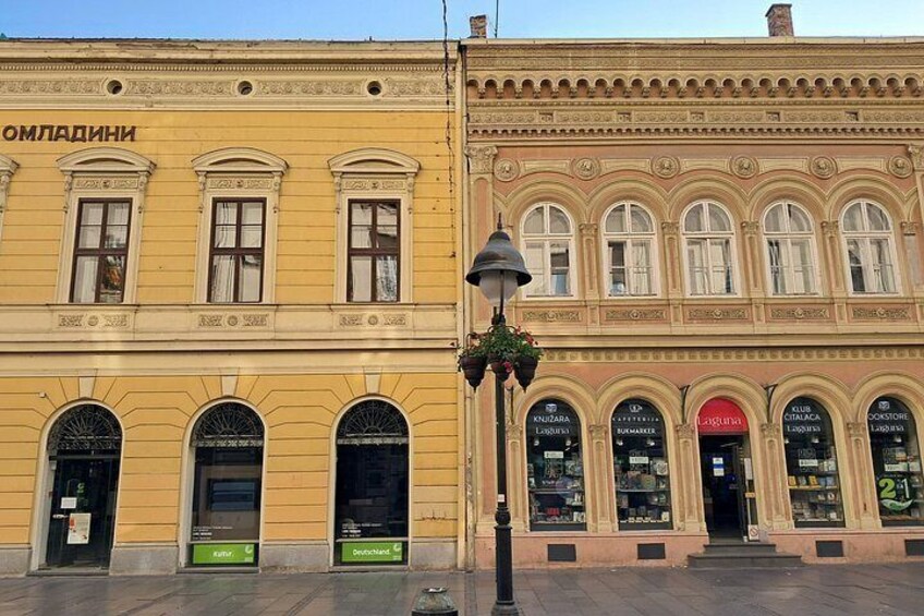 Two yellow buildings with arched windows and storefronts. 2
