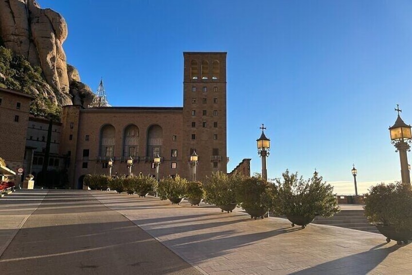 Un grand bâtiment doté de fenêtres en arc de cercle et d’une tour, entouré d’une place pavée agrémentée de lampadaires et de petits arbres. 5