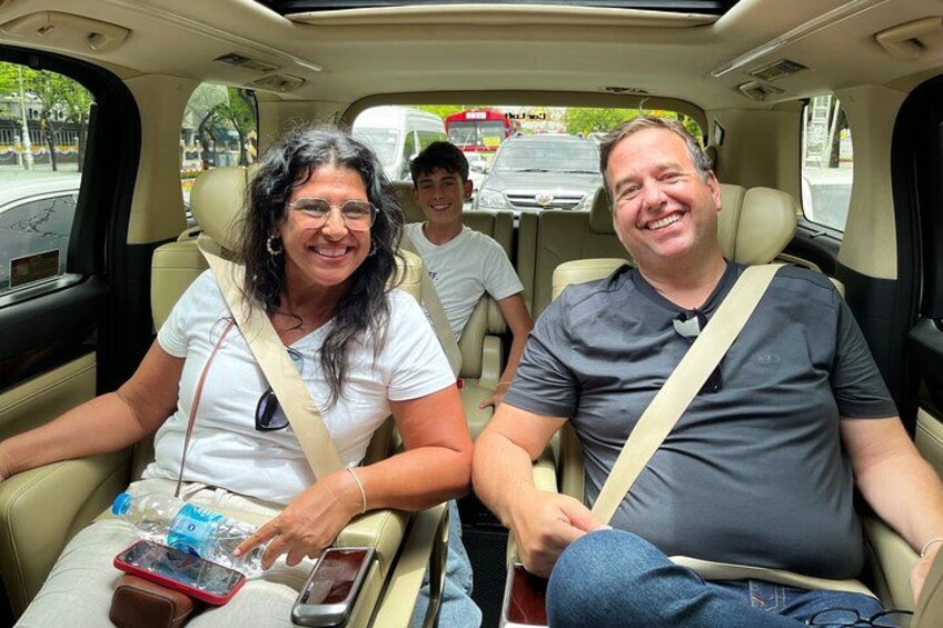 A car interior with two adults and a child seated, a child in the back seat, and a mobile phone on the seat in front. 2