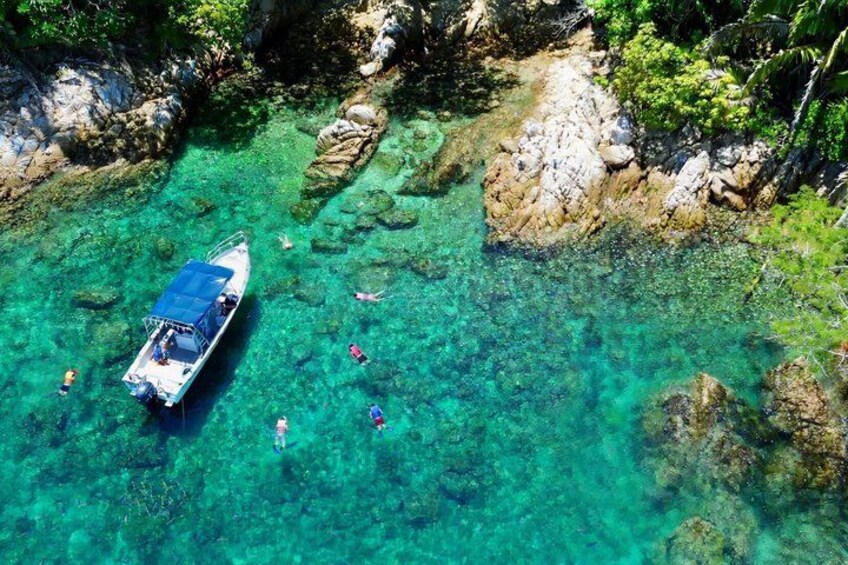 A boat anchored in clear turquoise waters surrounded by rocky terrain and lush greenery. 1