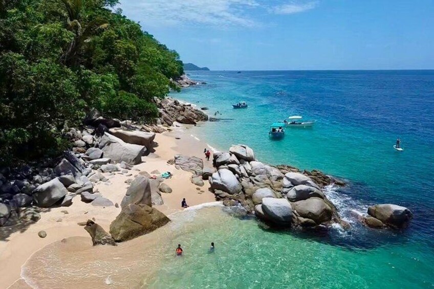 A beach with clear turquoise water, large rocks, and a forested area. 3