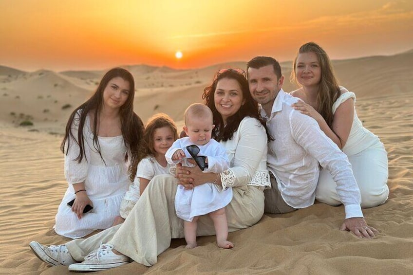 Una famiglia di cinque persone seduta sulle dune di sabbia al tramonto. 5