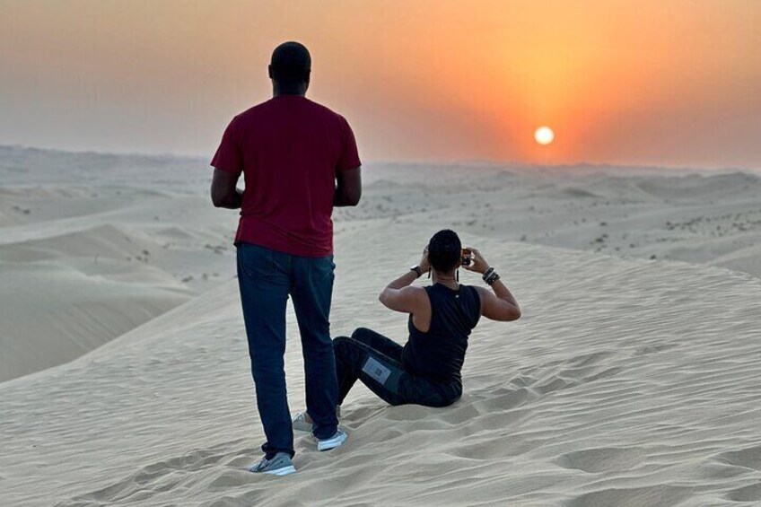 Due persone su una duna di sabbia nel deserto, con il sole al tramonto sullo sfondo. 4