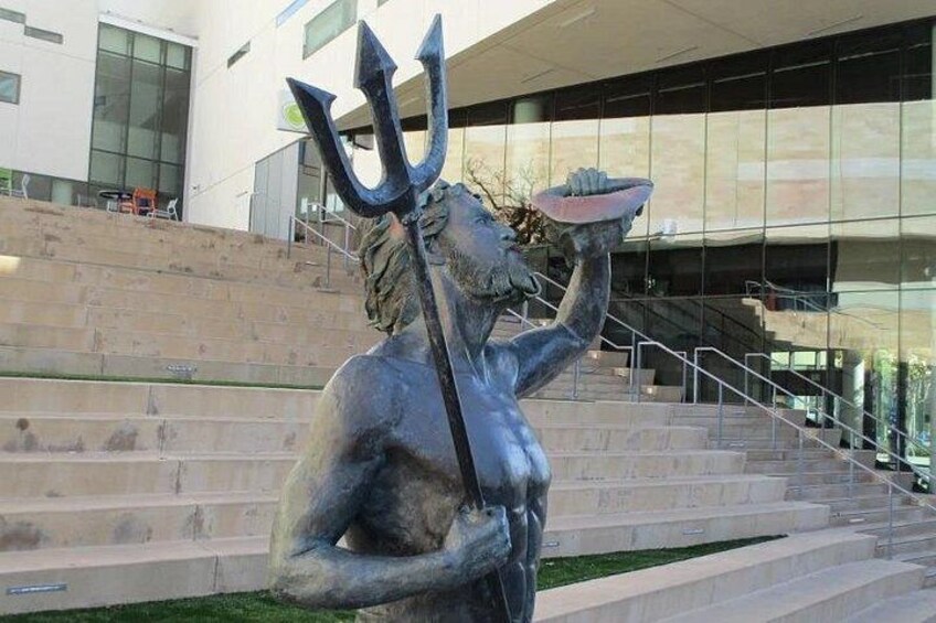 A statue of a sea creature holding a trident and a bowl, located in front of a modern building with steps. 2