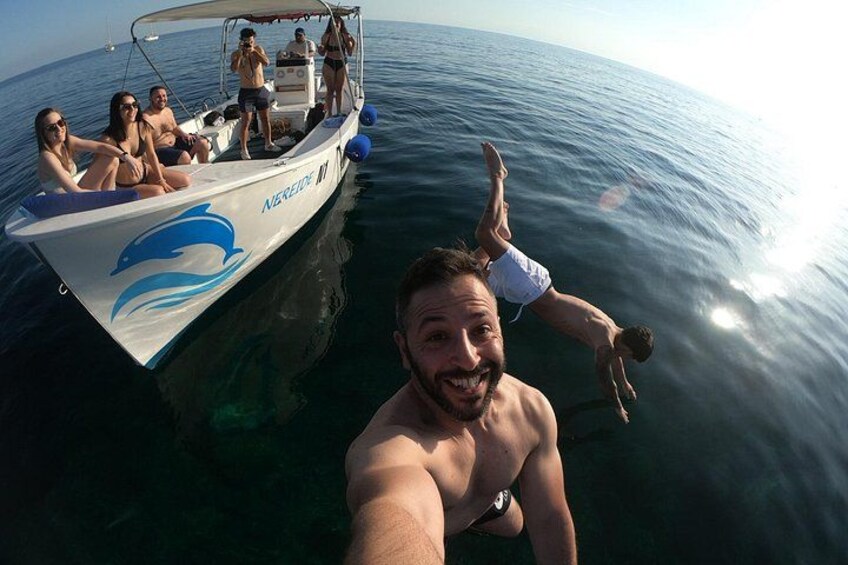 A boat with people on it, a person taking a selfie, and another person diving into the water. 3