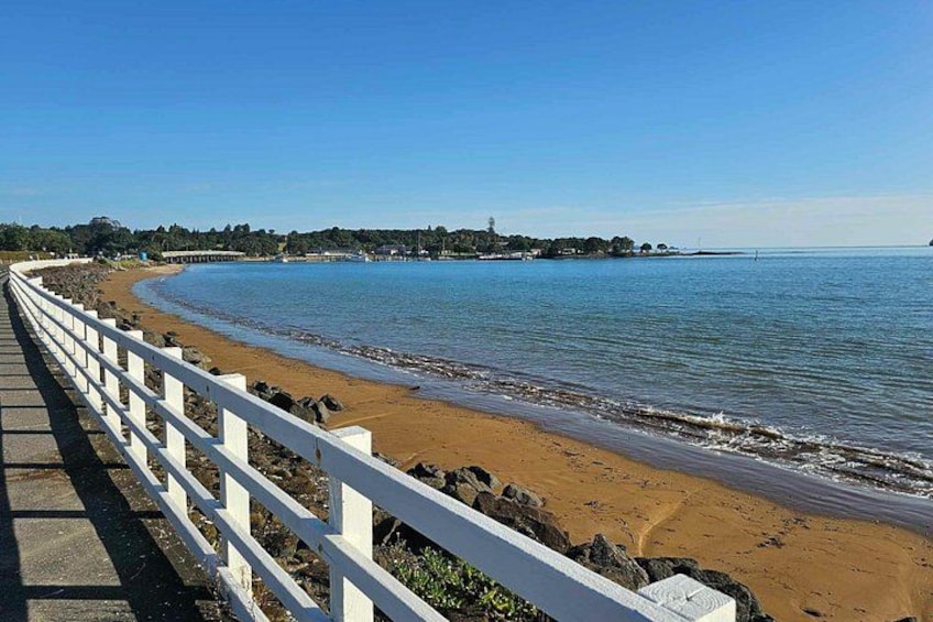 Une promenade en bord de mer avec une rambarde blanche, une plage de sable, une mer calme et un ciel dégagé. 2