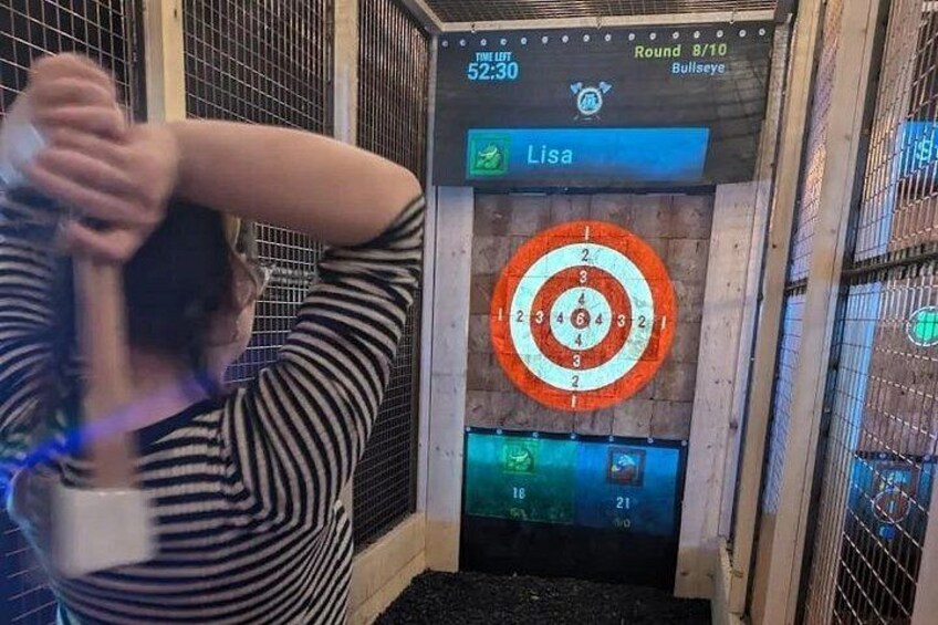 En person sigter mod en dartskive, med en scoretavle og et rosetmærke. 2