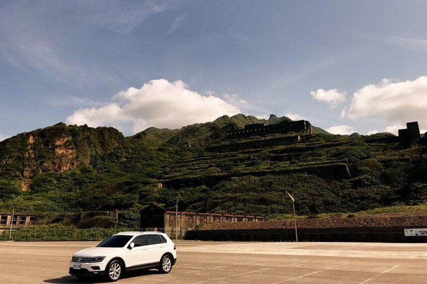 A white SUV parked in a lot with terraced hills and a clear sky in the background. 5