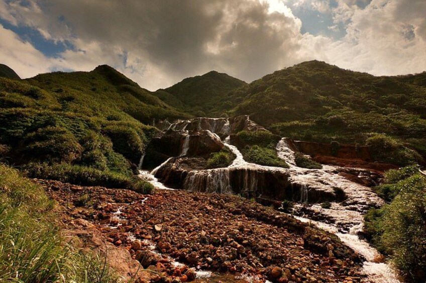 A waterfall cascading over rocky terrain surrounded by lush green hills. 4