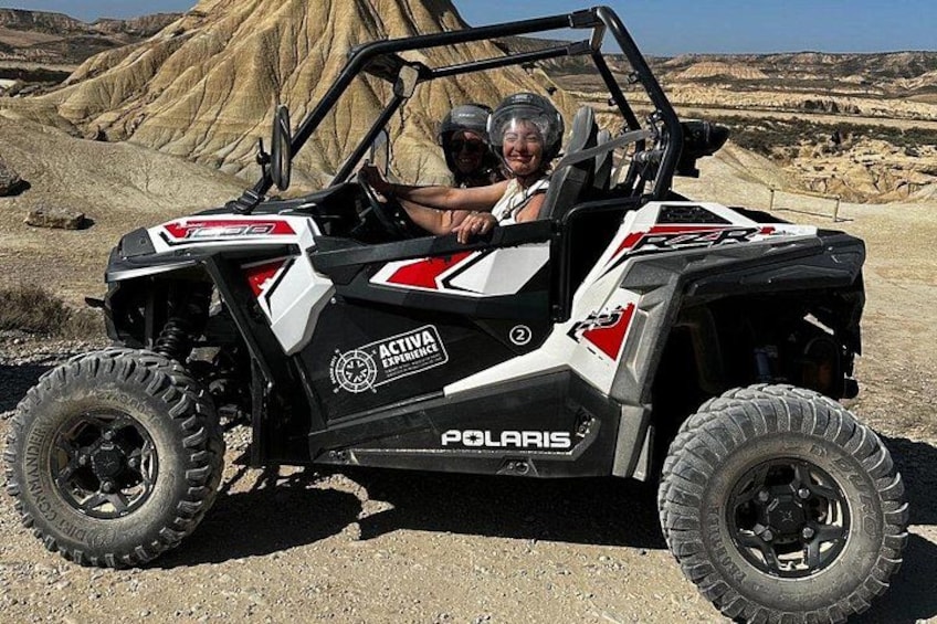 Un vehículo Polaris ATV con dos personas adentro, estacionado en un camino de tierra con un paisaje desértico al fondo. 1