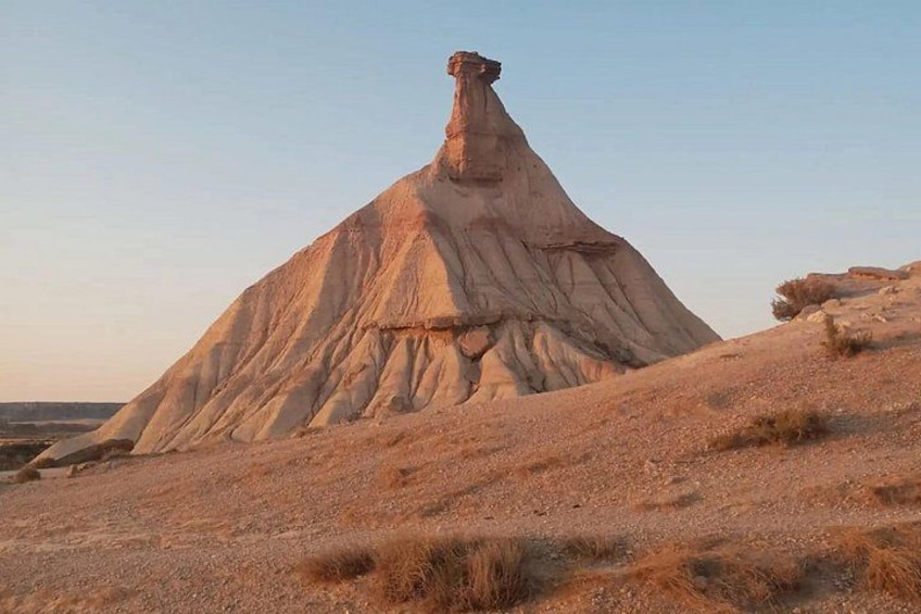 Una gran formación rocosa aislada, con una base estrecha y una cima ancha y plana, rodeada por un paisaje árido. 3