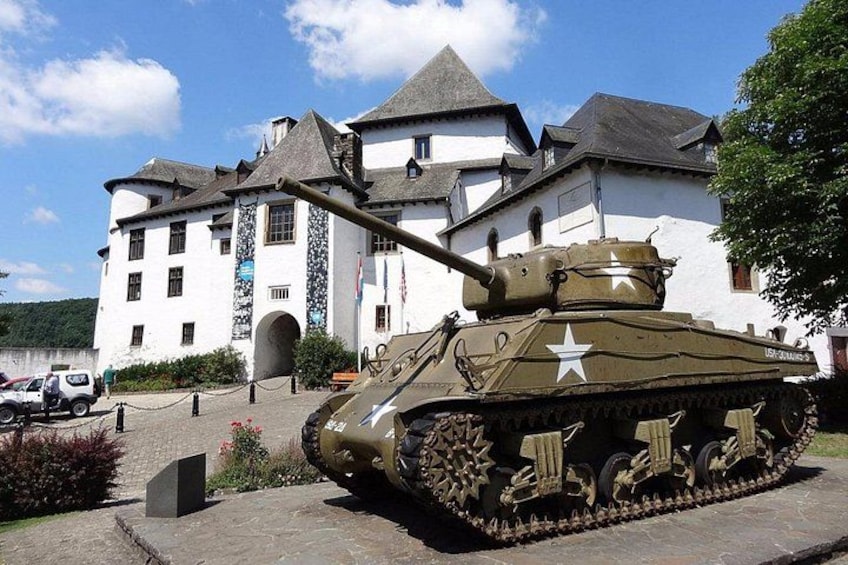 Un tanque militar frente a un edificio blanco con torreta. 1