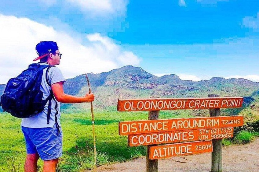 Un excursionista en el Mirador del Cráter de Olonongot, con un cartel que indica la distancia alrededor del borde y coordenadas. 1