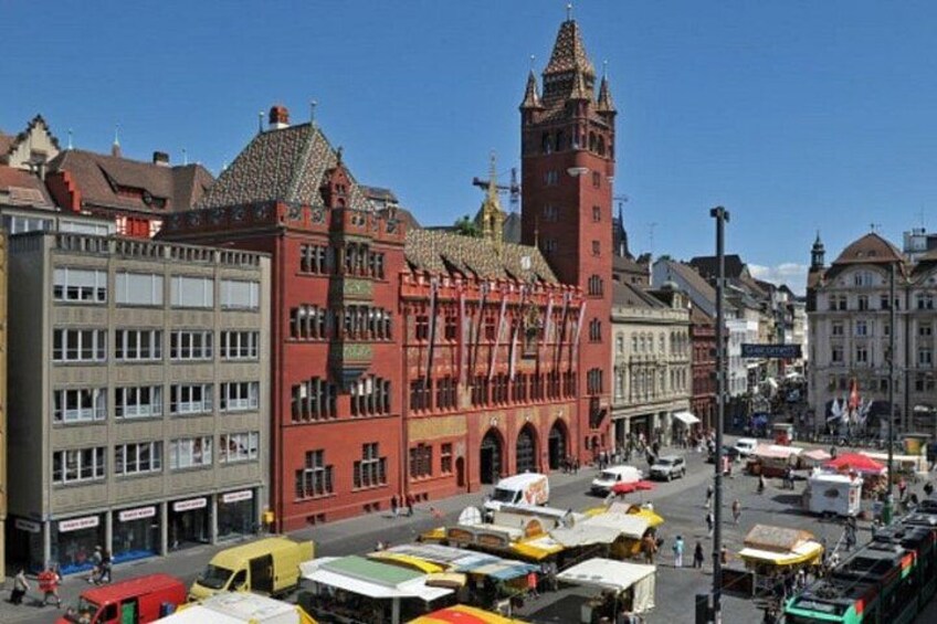 Una vivace strada con edifici storici, un'imponente torre dell'orologio e un'area mercato affollata. 2