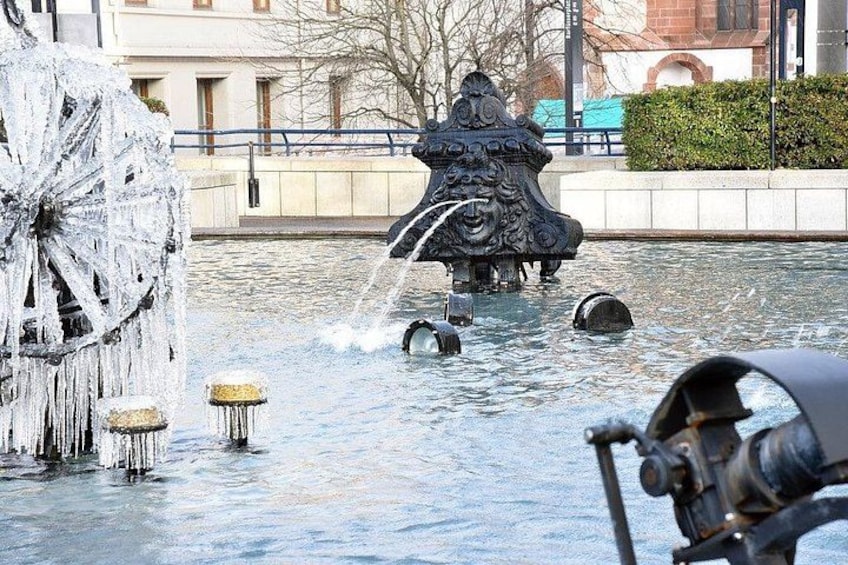 Una fontana di ghiaccio con una statua decorativa, una grande ruota ricoperta di ghiaccio e un ponte sullo sfondo. 5