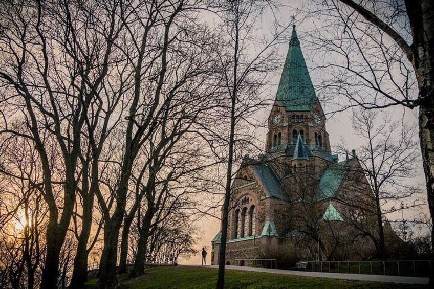 Una iglesia con una aguja alta y una torre del reloj, rodeada de árboles sin hojas. 1