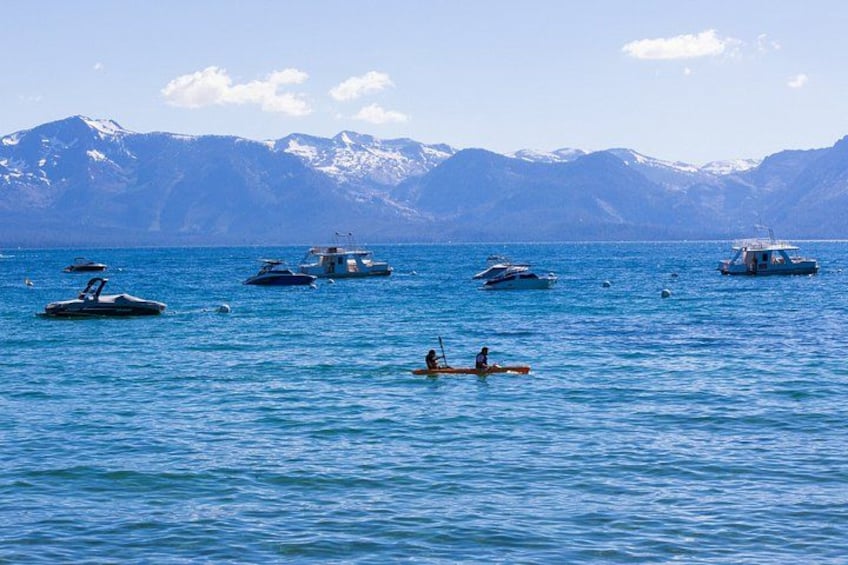A calm lake with several boats, a couple in a canoe, and snow-capped mountains in the background. 2