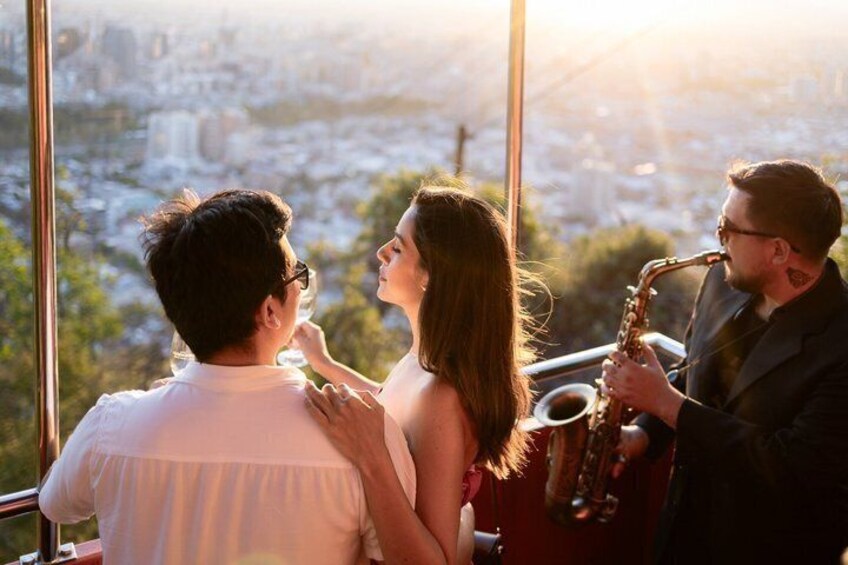 A couple standing by a window overlooking a cityscape, with a saxophonist playing in the foreground. 1