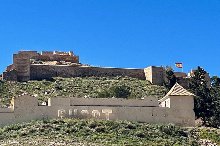 A fortified hilltop with a clear sky, a small building with a tiled roof, and a flag on top. 3