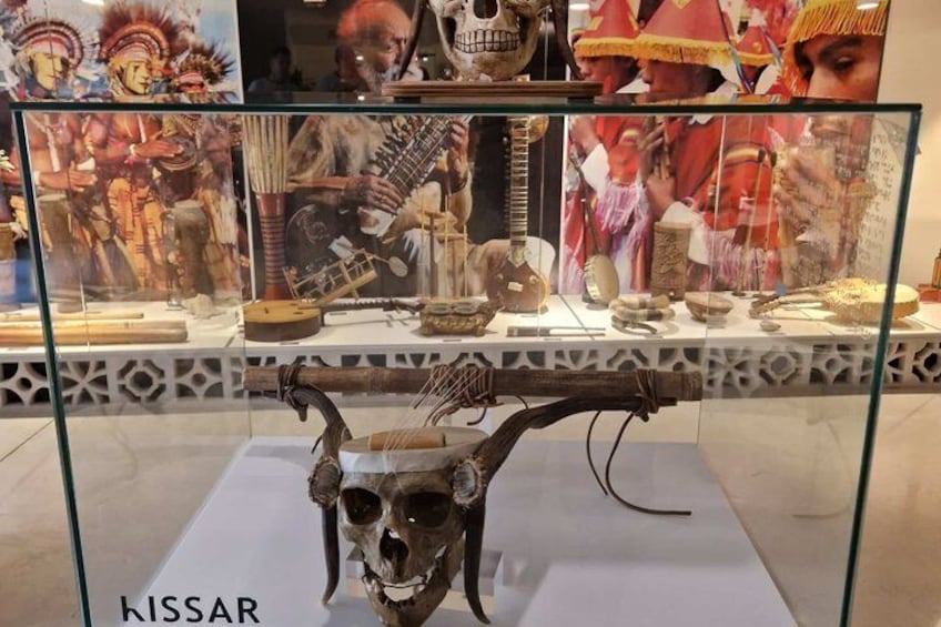 Eine Museumsvitrine mit Ausstellungsstücken, darunter ein Schädel, Musikinstrumente und kulturelle Artefakte. 3