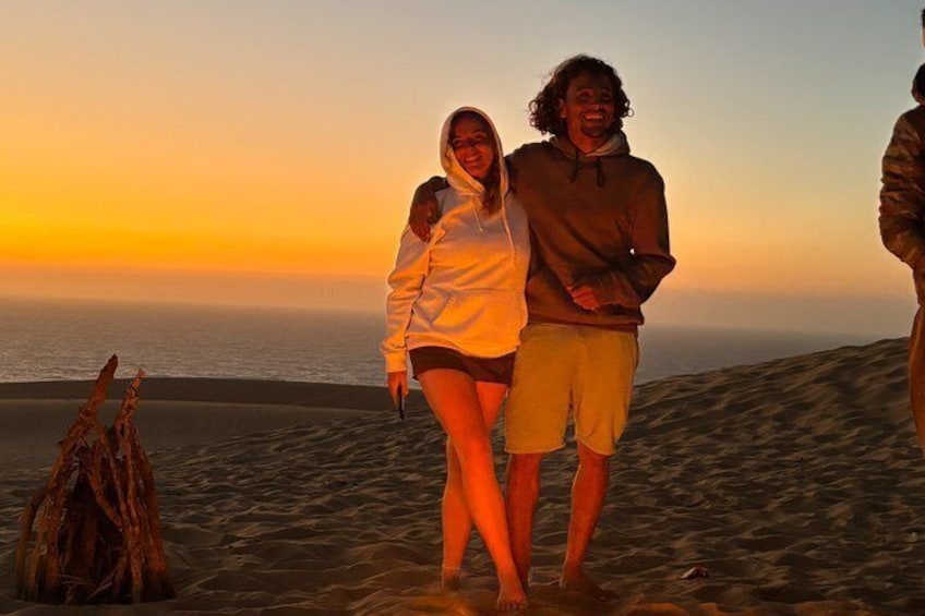 Un atardecer sobre un paisaje desértico con dunas de arena y una persona de pie al frente. 3