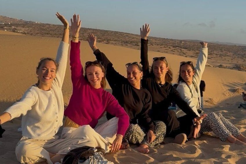 Un grupo de personas sentadas en una playa arenosa con los brazos levantados. 1