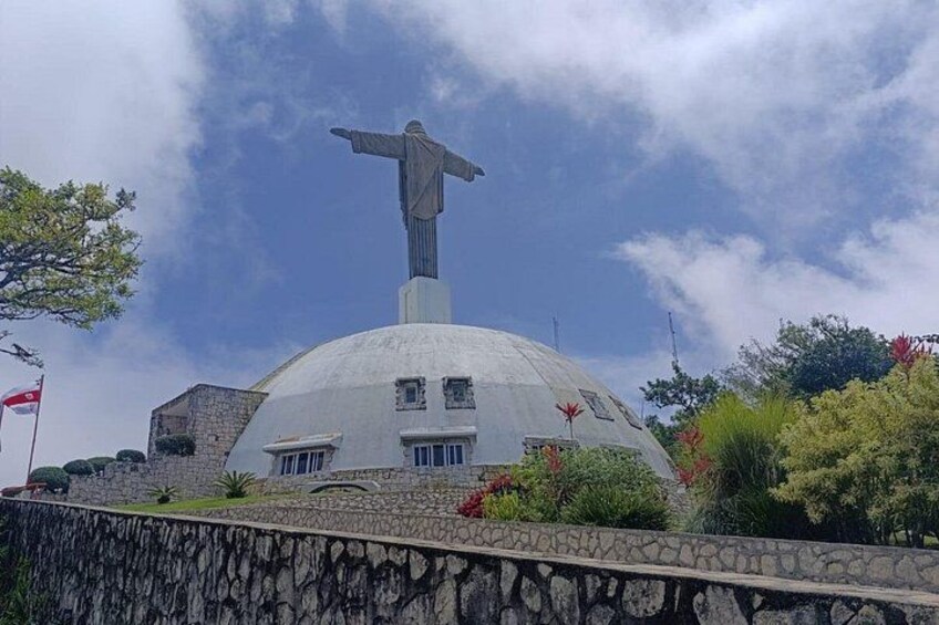 A large dome structure with a statue on top, surrounded by greenery and a stone wall. 1