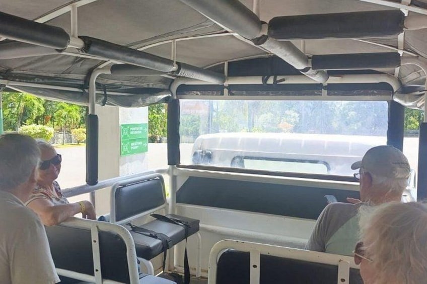 A bus interior with passengers seated, windows showing a road with a vehicle, and a green directional sign. 3