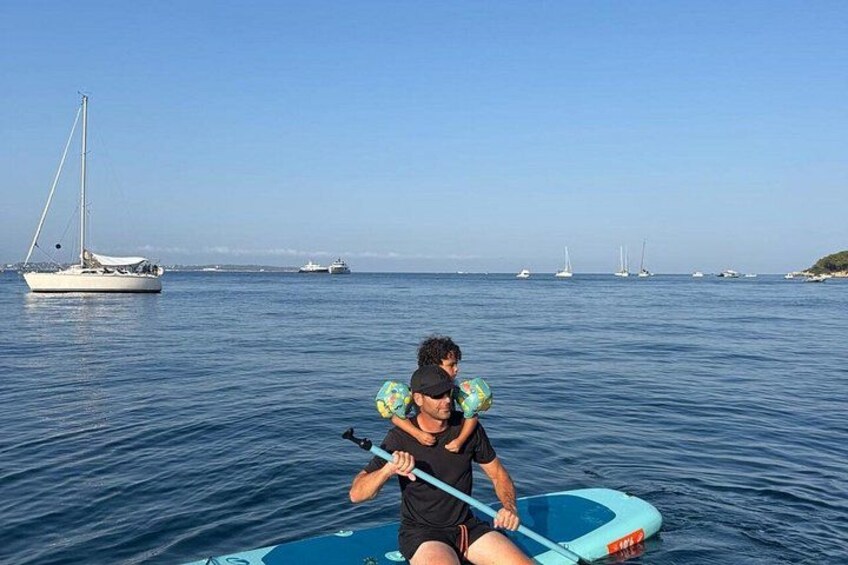 A person on a blue paddleboard in calm water with sailboats in the background. 2