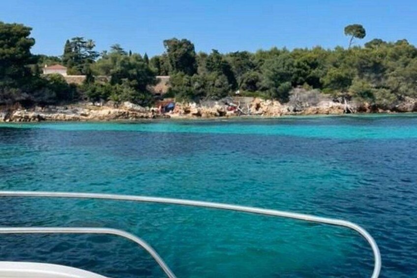 A coastal landscape with clear turquoise waters, a boat in the foreground, and a tree-lined shore with buildings in the background. 4