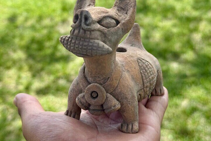 A hand holding a small, ancient-looking stone sculpture of a creature with a prominent nose and a circular eye. 4