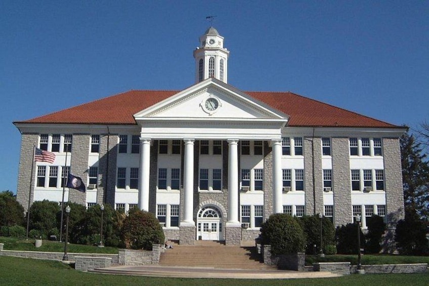 A large, historic building with a central clock tower, columns, and a red-tiled roof. 2