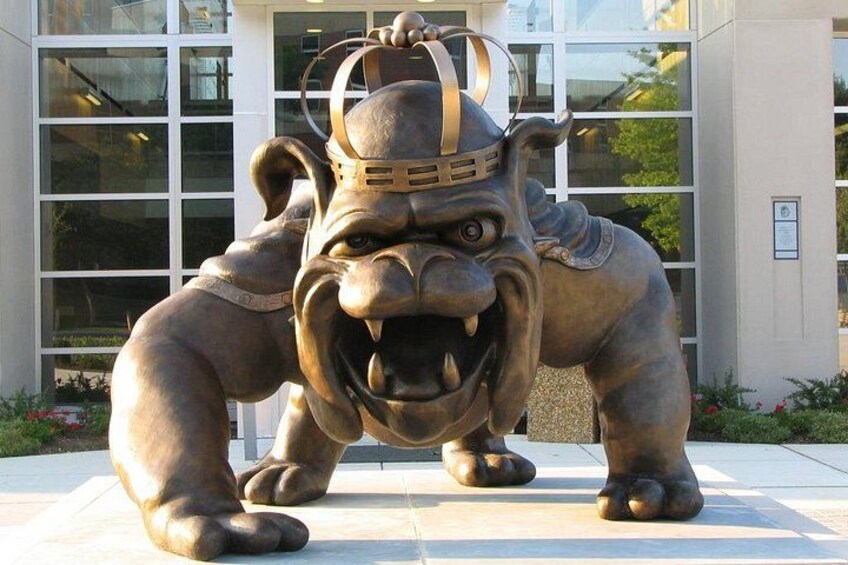 A bronze statue of a fierce animal with a crown, positioned in front of a building with large windows. 1