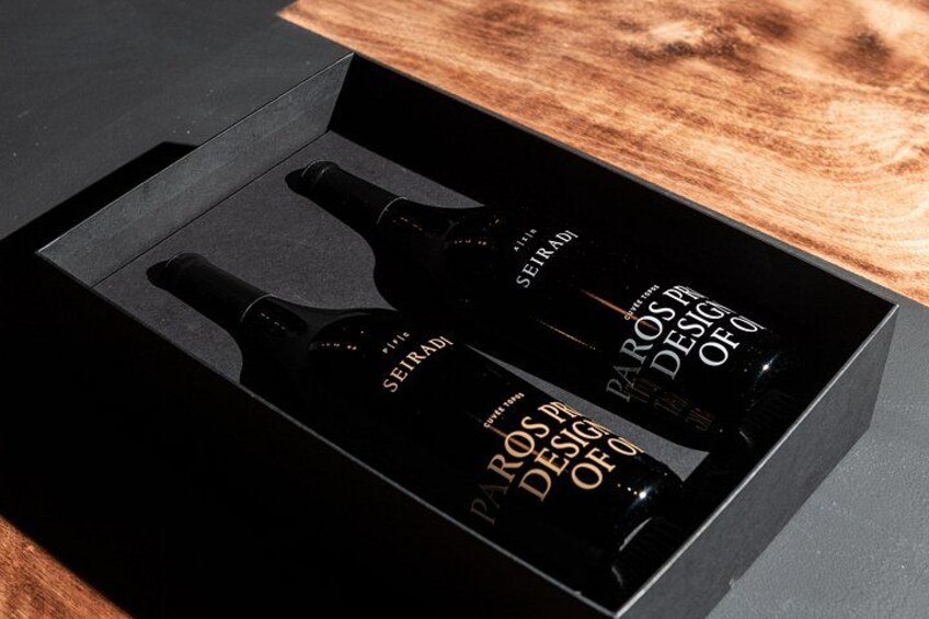 A black box with two bottles labeled 'SEIRADI' and 'PAROS DESIGN OF Q' on a wooden surface. 1