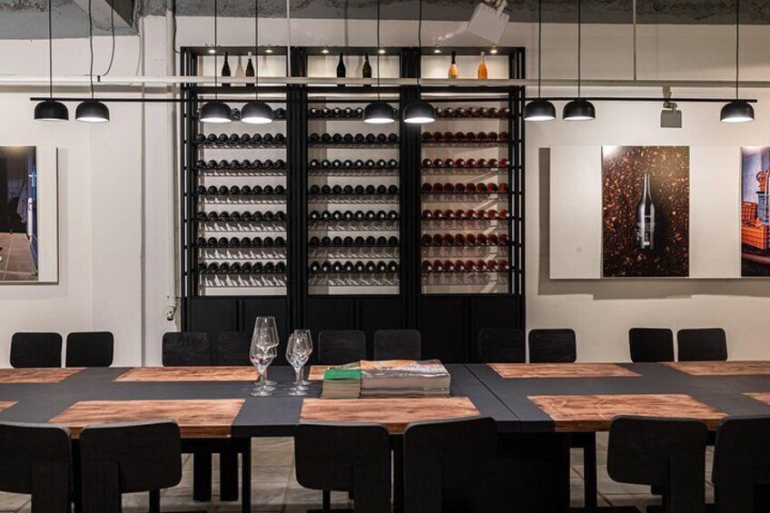 A conference room with a long table, chairs, wine bottles, and wine glasses. 1