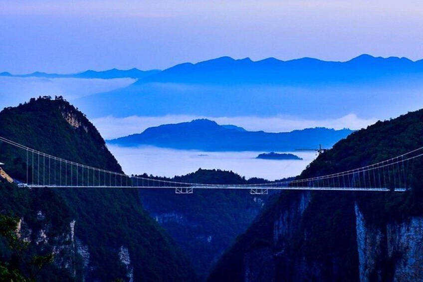 A suspension bridge over a deep valley with mountains in the background. 2