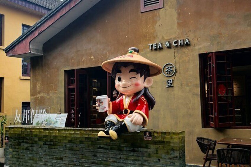 Een standbeeld van een personage met een kopje, voor een gebouw met de tekst 'TEA & CHA'. 2