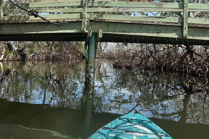 Een kajak op een kalm wateroppervlak met een houten brug erboven. 5