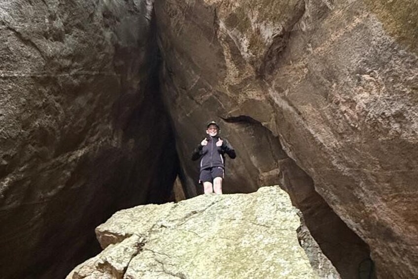 A person standing on a rock ledge in a narrow canyon with large rock formations. 4