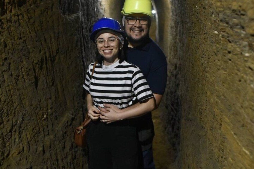 Two people in a narrow, rocky tunnel with one wearing a blue helmet and the other a yellow helmet. 3