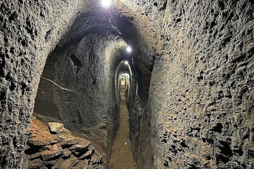 A narrow, rocky tunnel with a light source at the end. 1