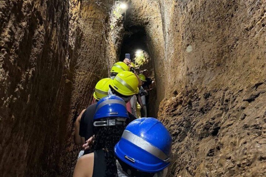 A group of people in hard hats and safety gear inside a narrow, rocky tunnel. 2